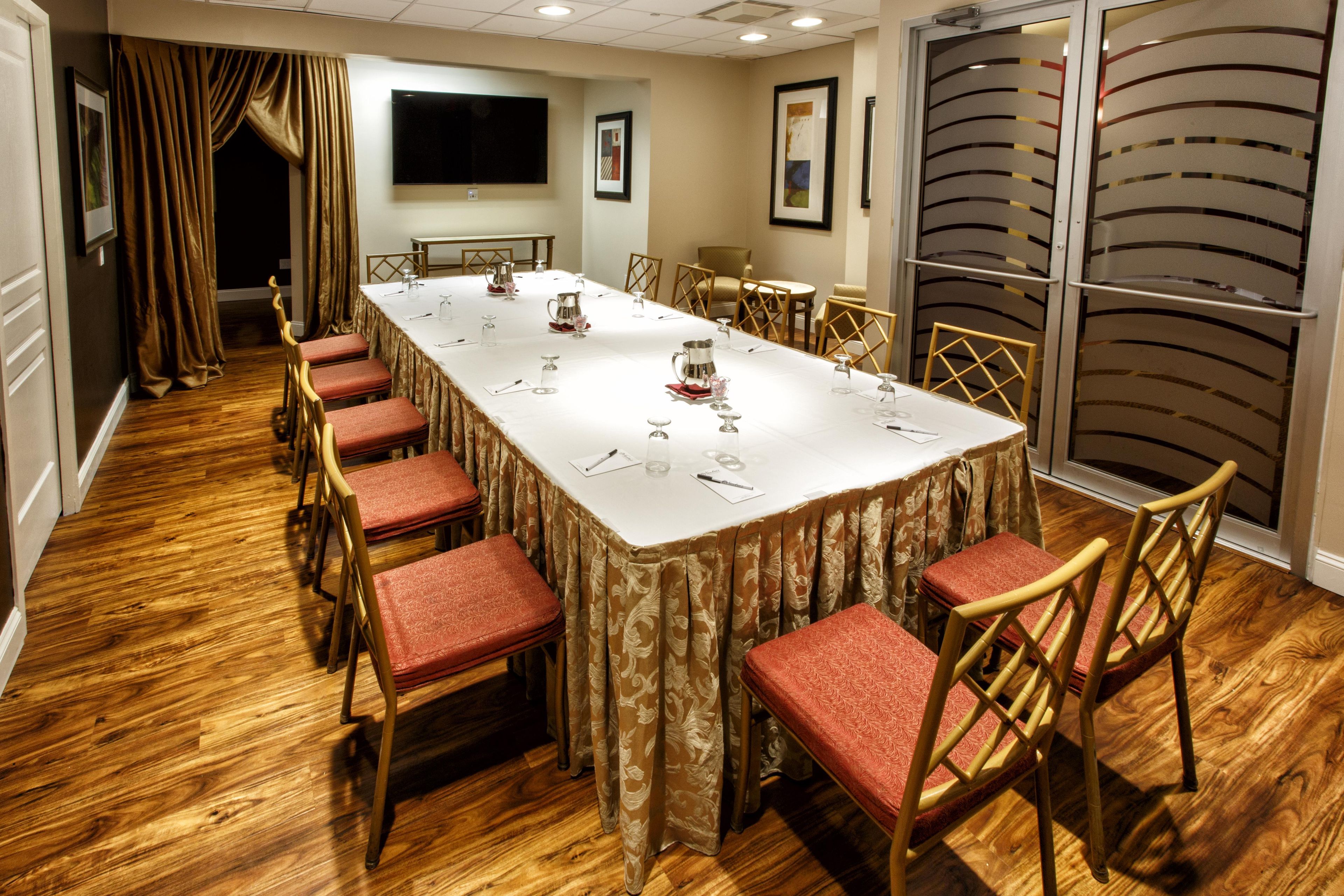 Un salón de conferencias con una mesa larga, sillas y una pantalla de televisión.
