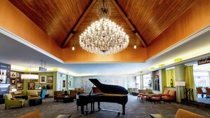 A spacious lobby with a grand piano, comfortable seating, and a large chandelier.