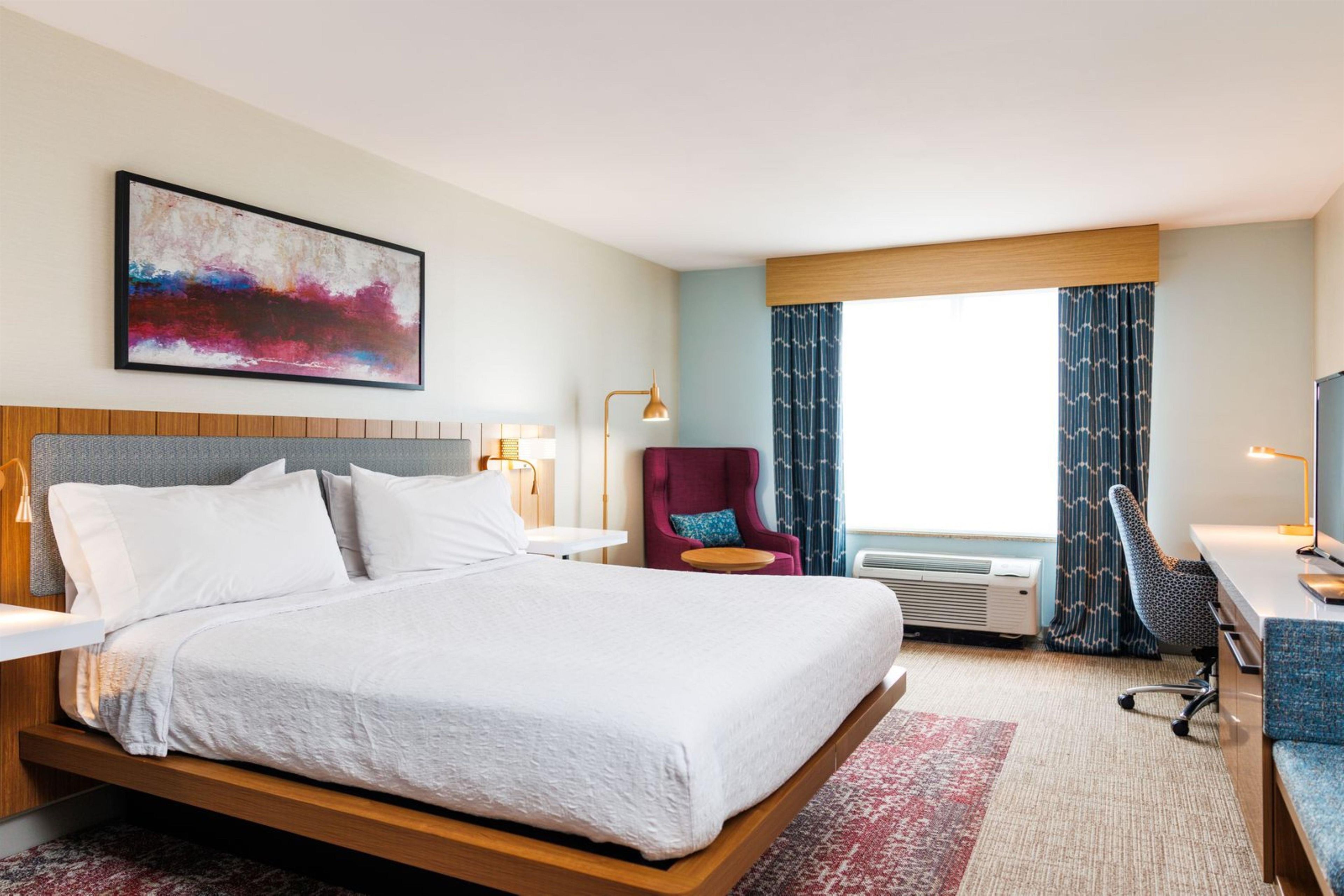Une chambre d’hôtel avec un grand lit, un bureau, une chaise, une télévision et une fenêtre avec des rideaux.