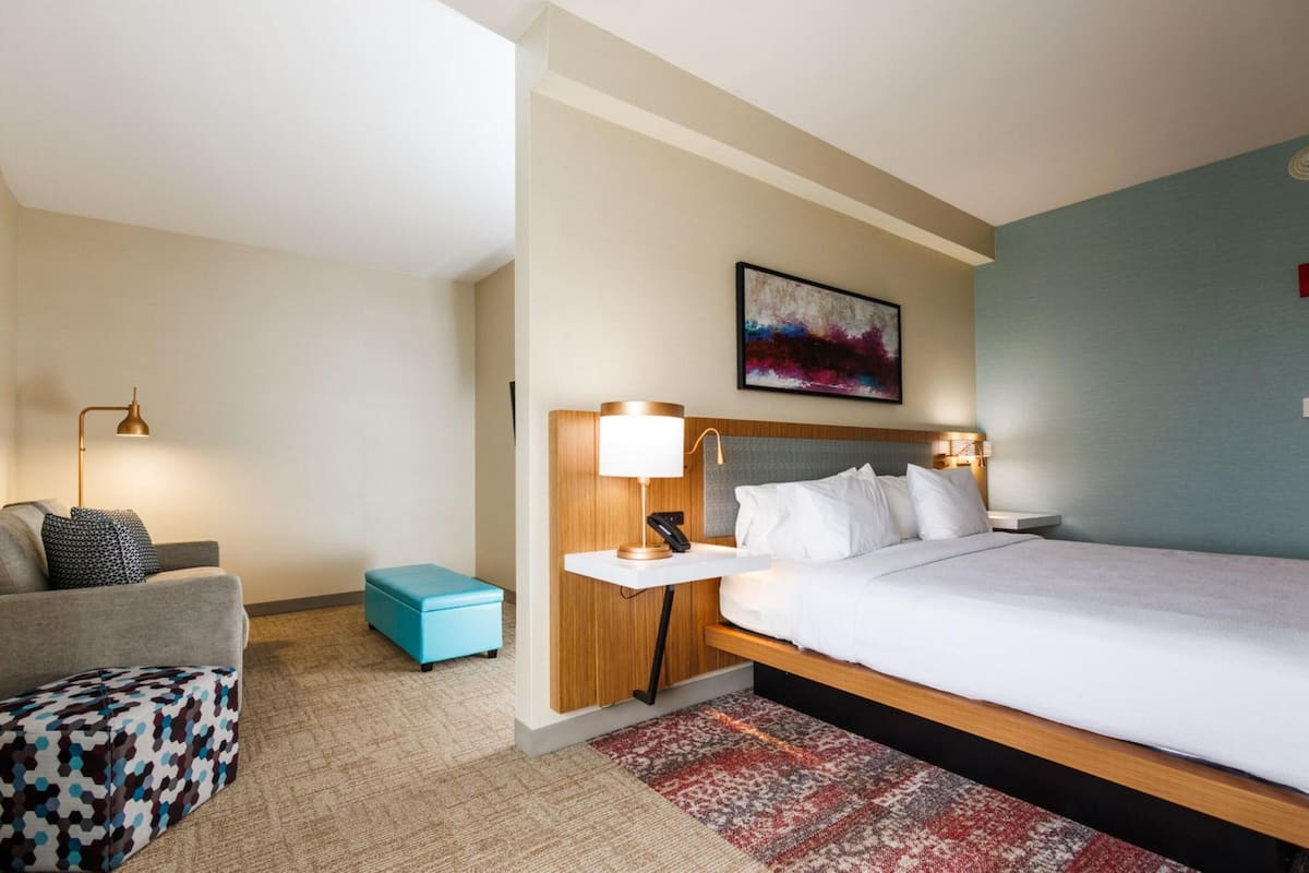 Una habitación de hotel con cama, escritorio, silla, sofá y un pequeño reposapiés.
