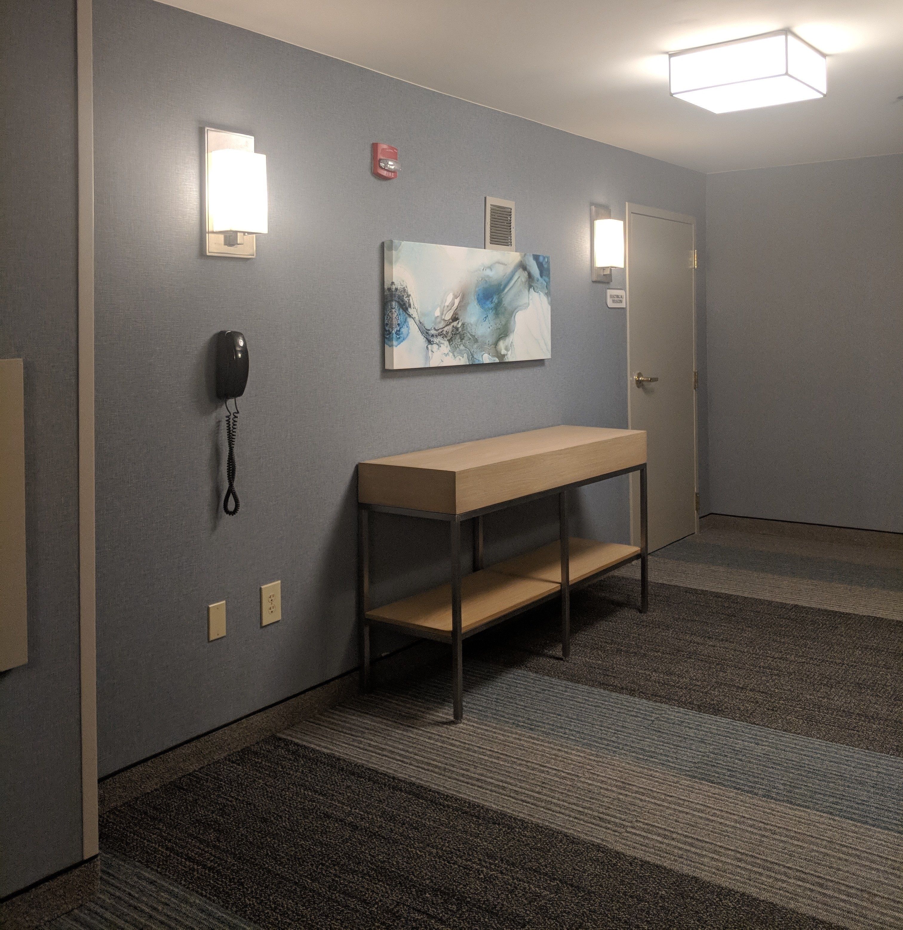 A hotel hallway with a wooden bench, a phone, and a painting on the wall.