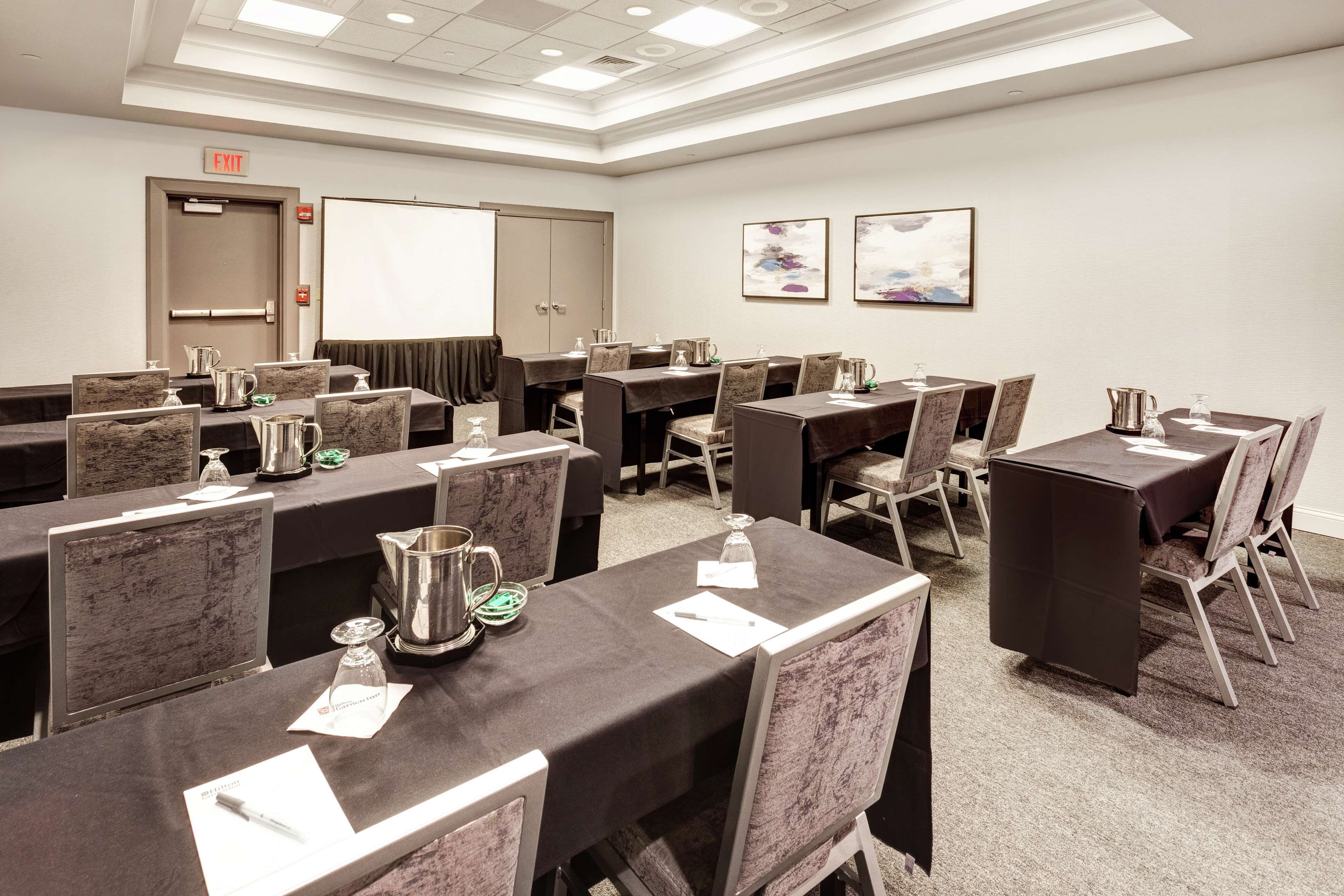 A conference room with multiple tables, chairs, and presentation screens.