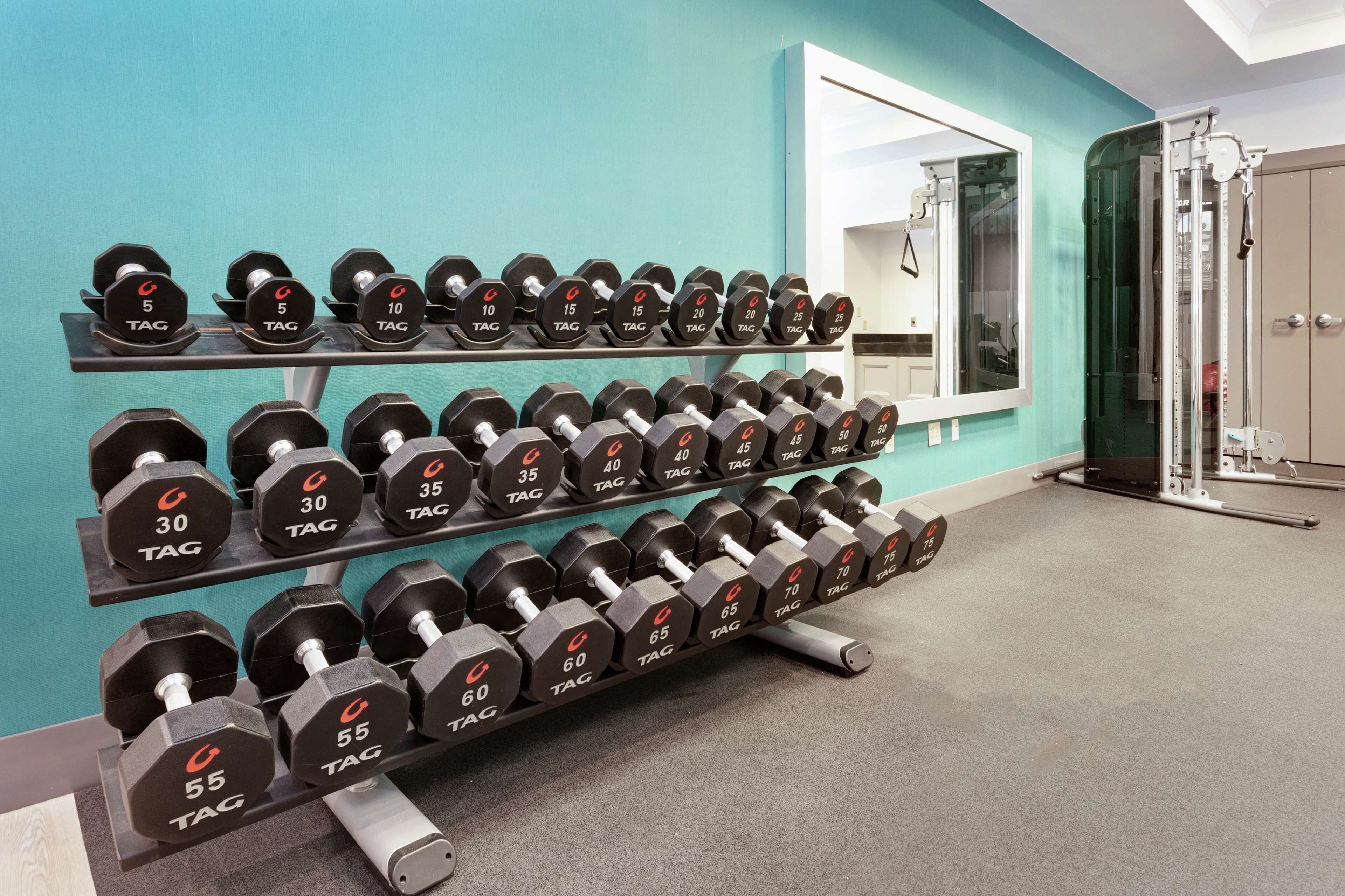 Un gimnasio con estantes para pesas, un espejo y una puerta a vestuarios.