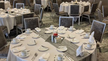 A conference room with multiple round tables set for a meeting, equipped with nameplates, chairs, and a central floral arrangement.