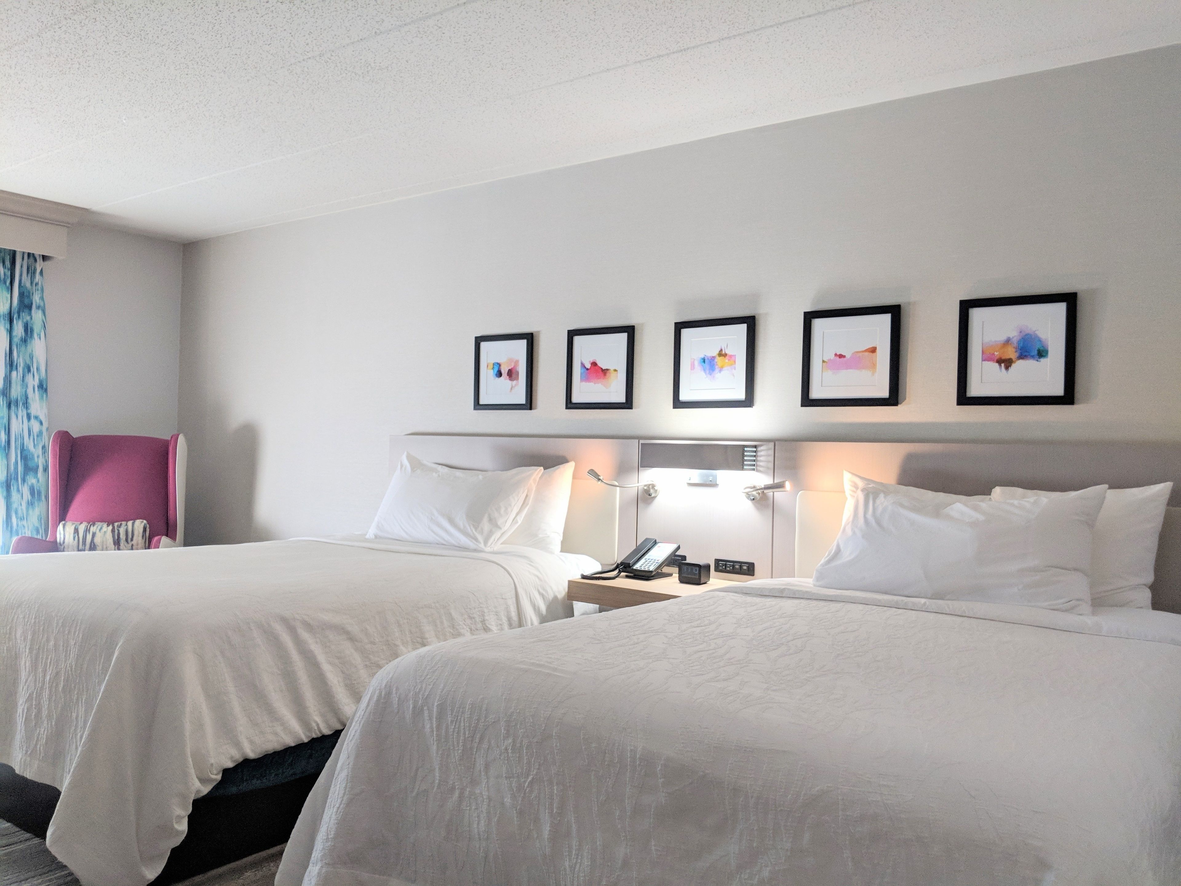 A hotel room with two beds, a desk with a phone, and framed artwork on the wall.
