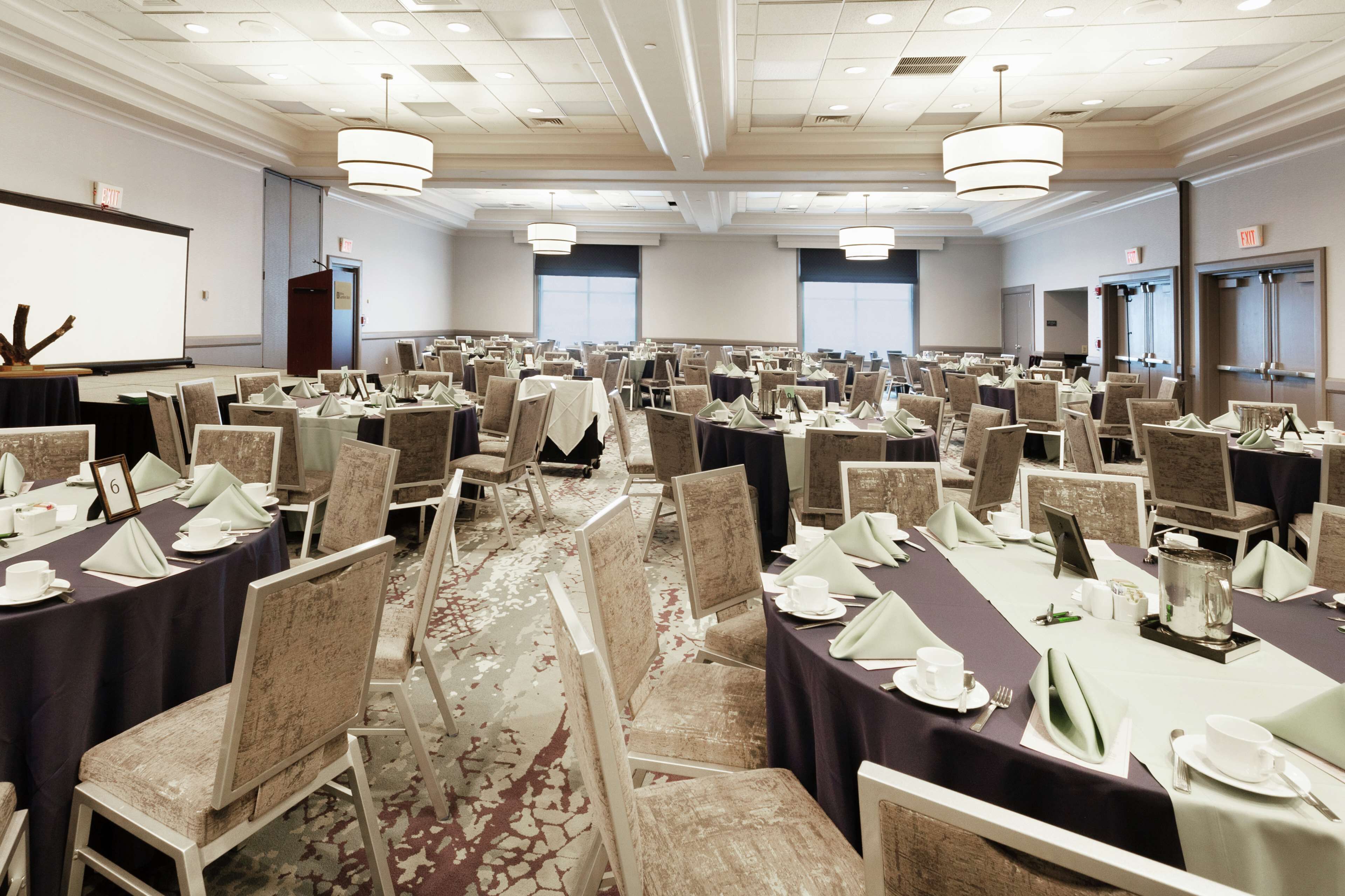 A large conference room with rows of tables set for a meeting, equipped with nameplates, chairs, and table settings.