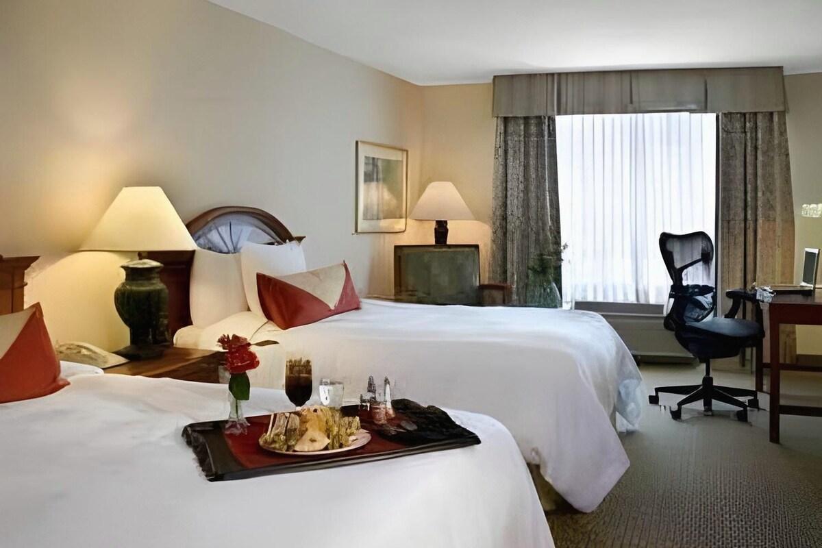 A hotel room with two beds, a desk, a chair, and a window with curtains.
