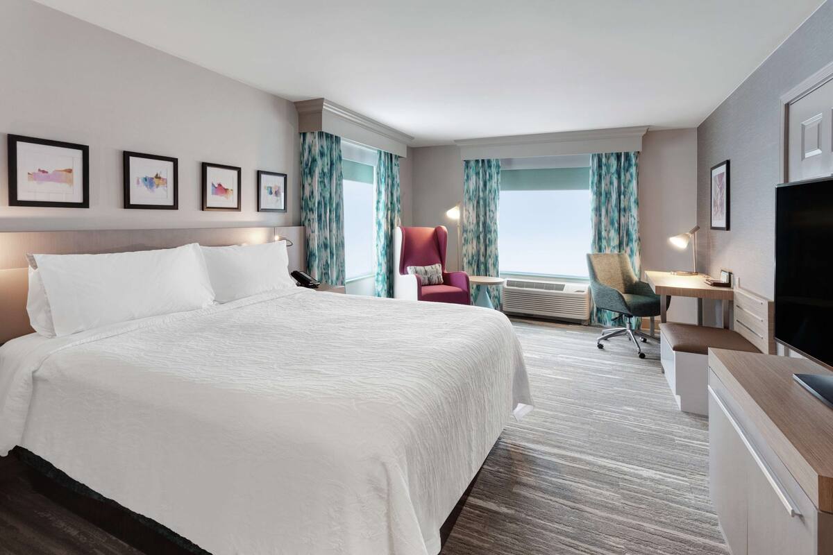 A hotel room with a large bed, a desk with a chair, a TV, and a window with curtains.