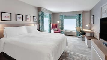 A hotel room with a large bed, a desk with a chair, a TV, and a window with curtains.