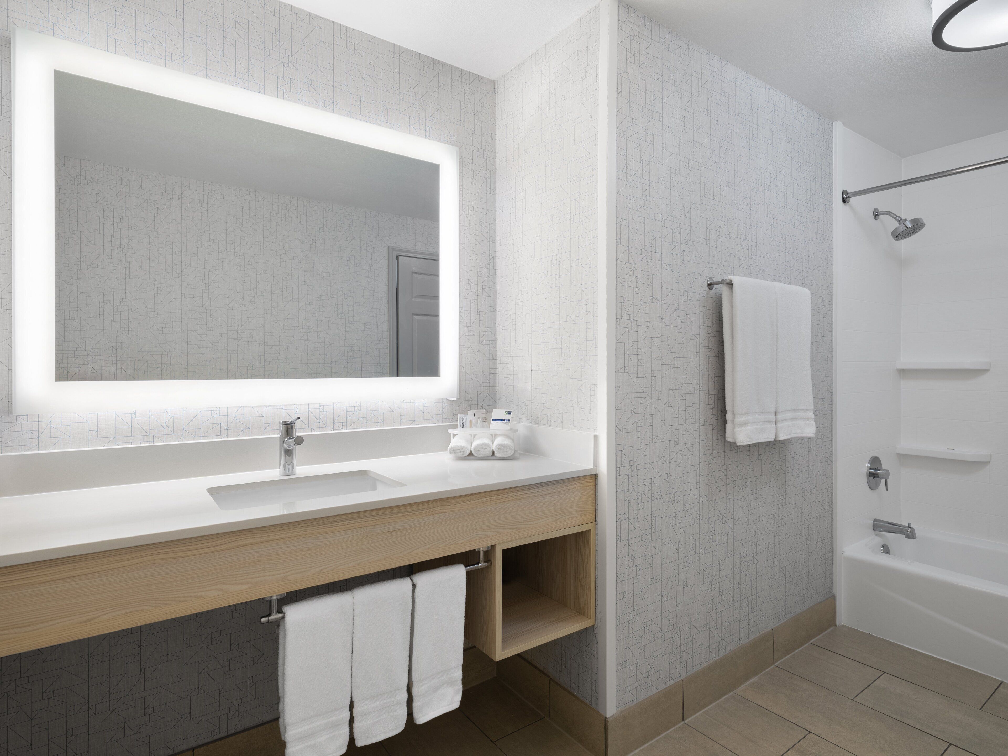 Un baño moderno con un espejo grande, un lavabo, una ducha y un perchero para toallas.