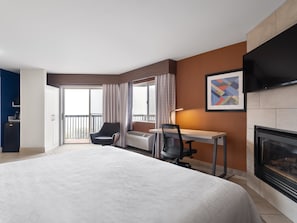 Una habitación de hotel con una cama grande, un escritorio, una silla, una chimenea y un televisor.