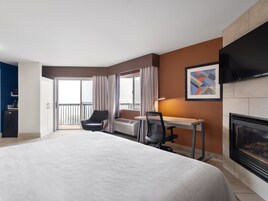 Una habitación de hotel con una cama grande, un escritorio, una silla, una chimenea y un televisor.
