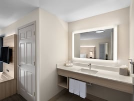 Un baño moderno con un espejo grande, un lavamanos y un televisor montado en la pared.