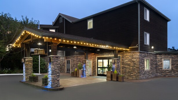 A large, dark wooden building with a stone facade, a covered entrance area with string lights, and a well-maintained outdoor space with potted plants. - Holiday Inn Express Ft Bragg by IHG (Fort Bragg)