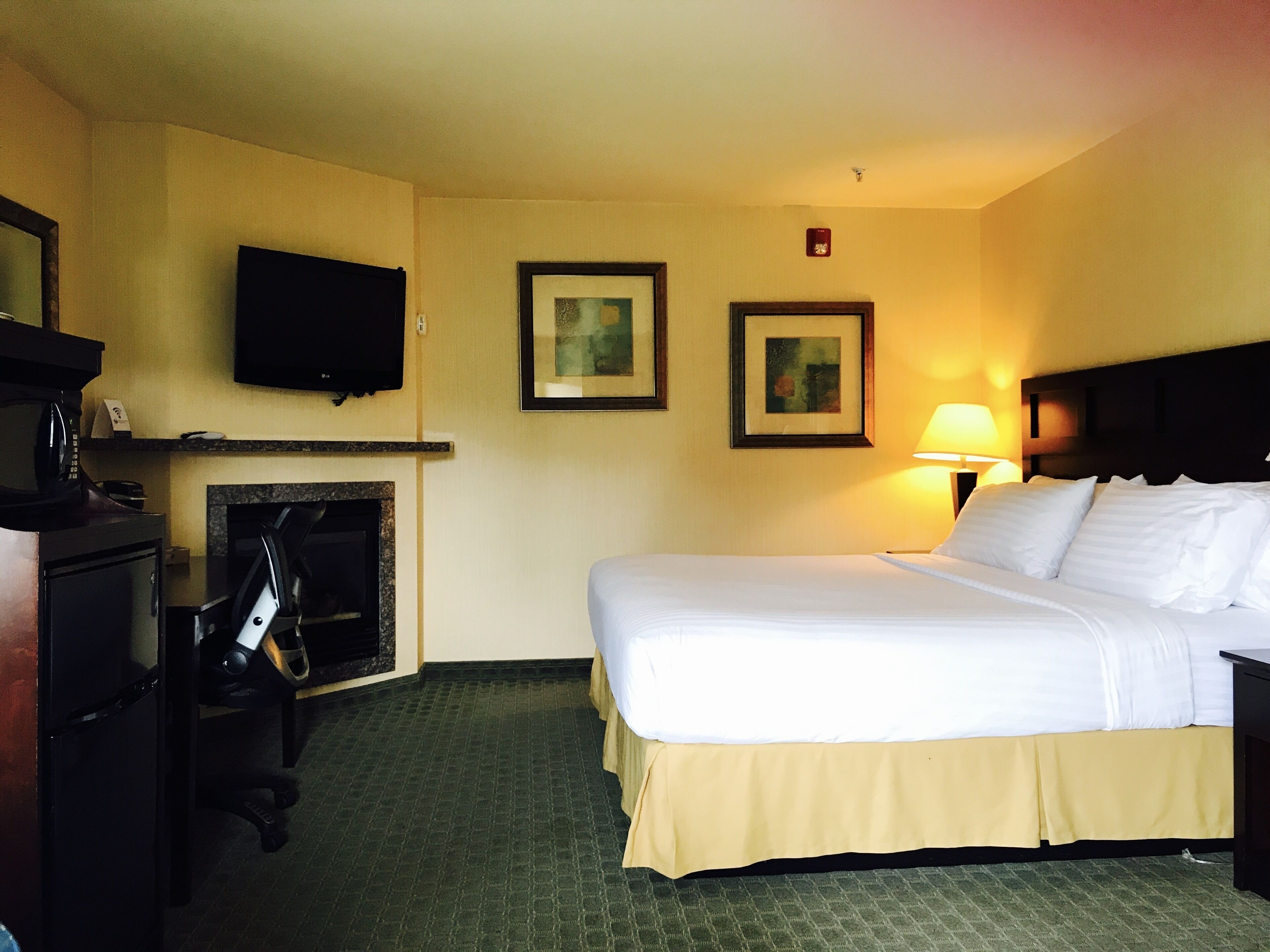 A hotel room with a bed, a television, a fireplace, and framed pictures on the wall.