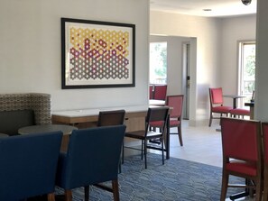 Enjoy meals in this stylish dining area with a long table and comfortable chairs, surrounded by a geometric patterned artwork and a view of the outdoors.