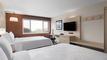 A hotel room with two beds, a desk, a chair, a TV, and a window with a view of the outdoors.