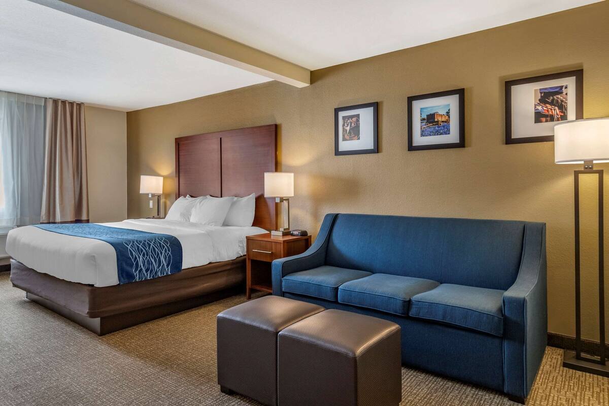 Una habitación de hotel con una cama grande, un sofá azul, una mesita pequeña y dos lámparas de pared.