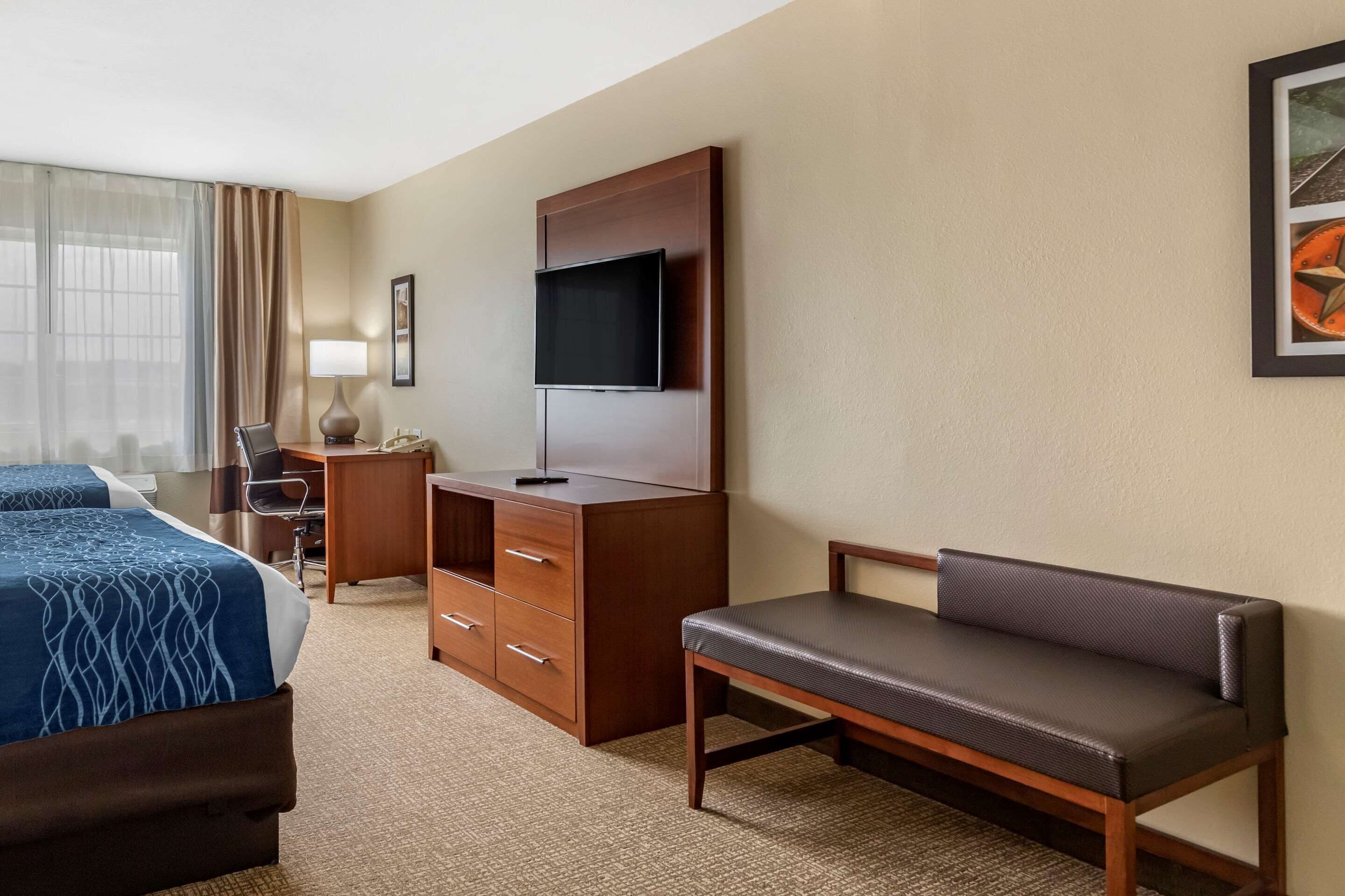 A hotel room with two beds, a desk, a chair, a TV, and a sofa.
