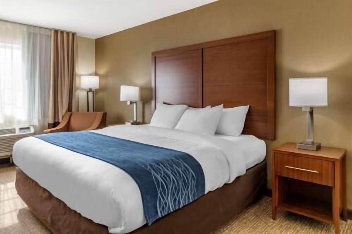 Una habitación de hotel con una cama grande, dos lámparas de noche, una mesita de noche de madera y una silla.