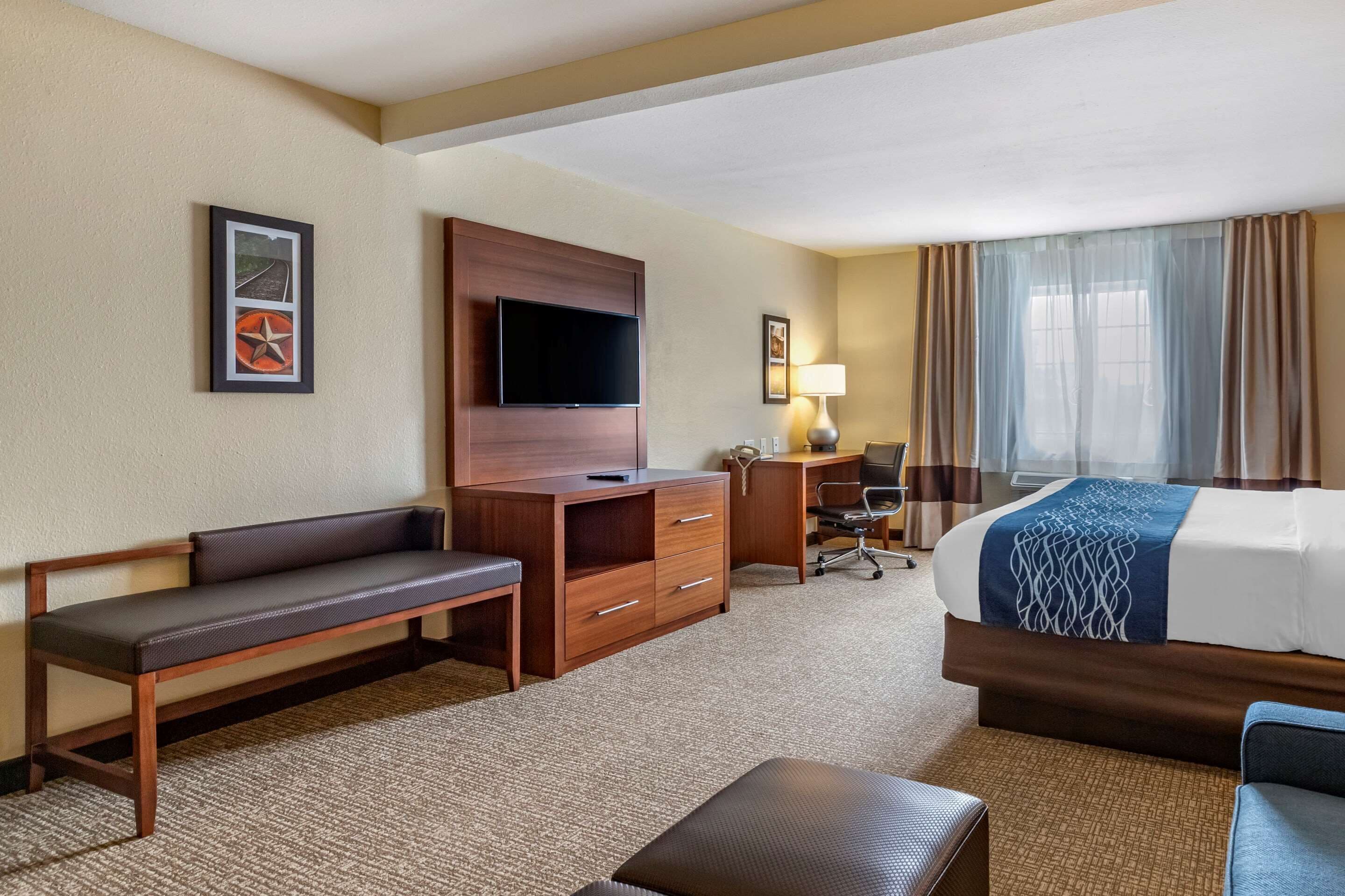 Habitación de hotel con cama, escritorio, silla, banca, televisor y lámpara.