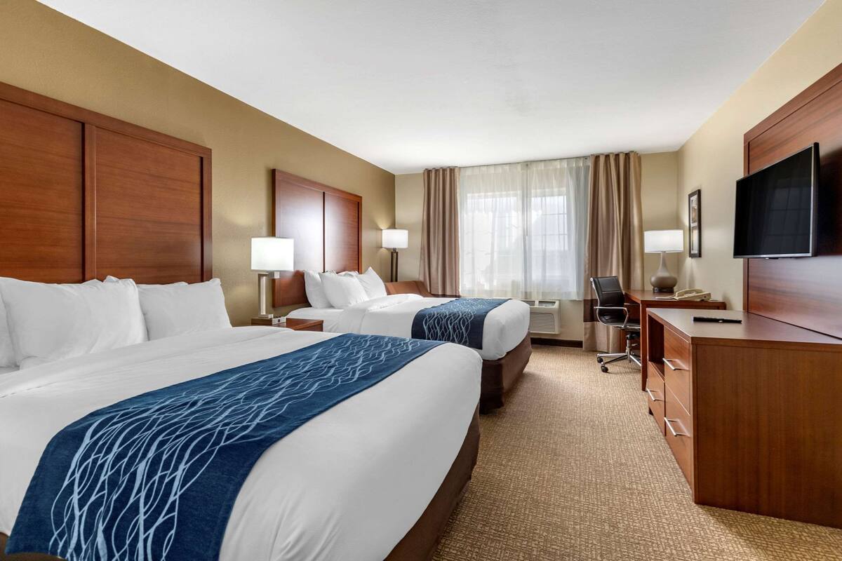Habitación de hotel con dos camas, un escritorio, un televisor y una ventana con cortinas.
