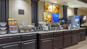 Mostrador de buffet con diversos alimentos, una máquina de café y un cartel que indica usar un plato limpio.