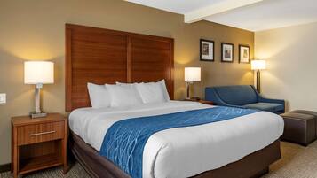 A hotel room with a large bed, a nightstand, a desk, a chair, and a lamp.