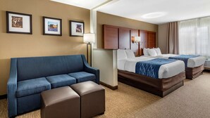Habitación de hotel con un sofá azul, dos camas con ropa de cama blanca y azul, un cabecero de madera y cuadros enmarcados en la pared.