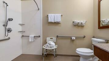 Une salle de bain équipée d’une douche, de toilettes, d’une barre d’appui et d’un siège accessible aux personnes en fauteuil roulant, ainsi que de serviettes.