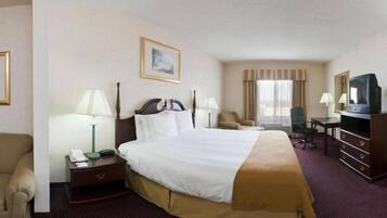 A hotel room with a large bed, bedside lamps, a desk with a chair, a television, and a window with curtains.