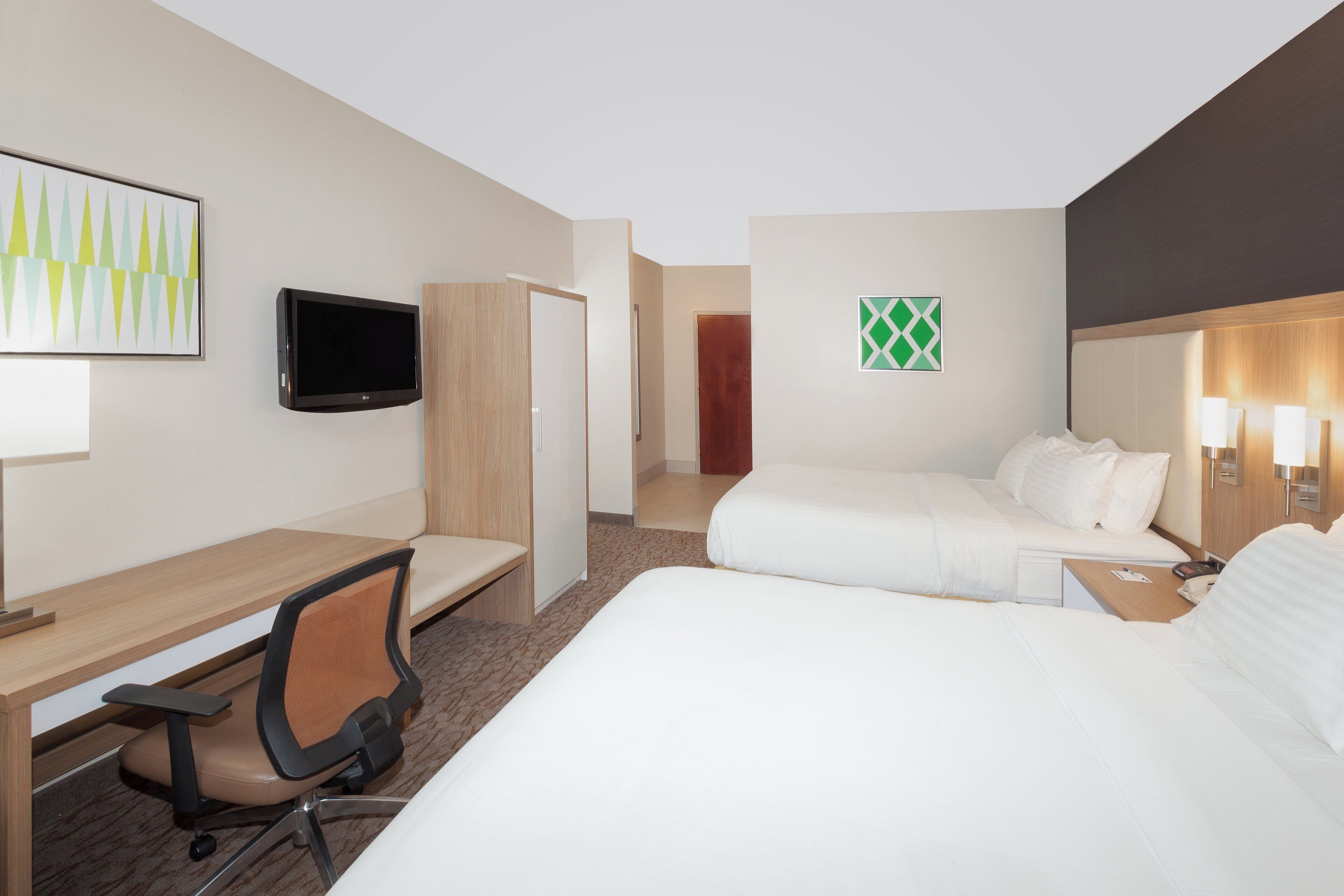 A hotel room with a bed, a desk, a chair, a television, and a door.