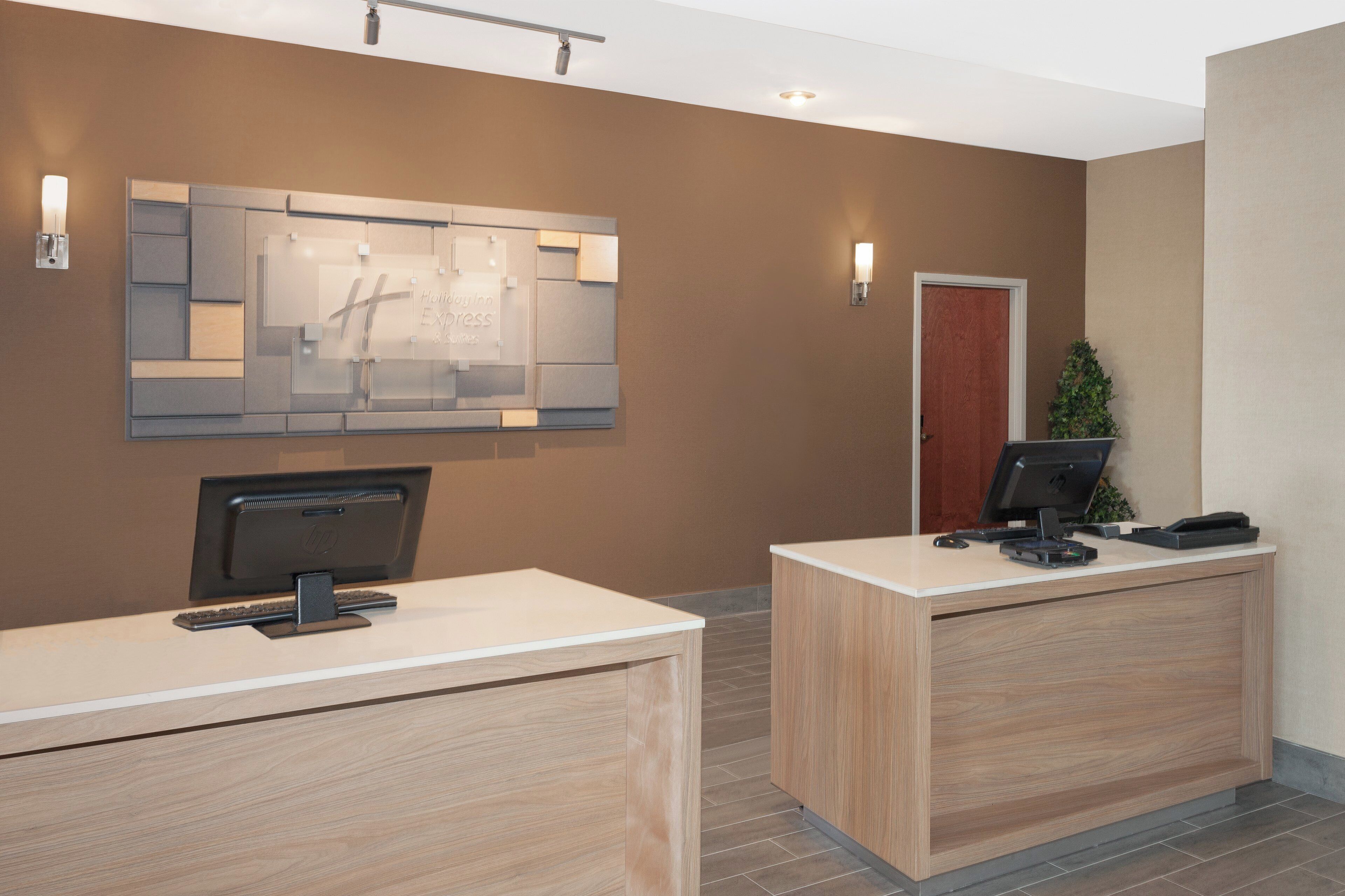 A reception desk with a computer, a plant, and a door in the background.