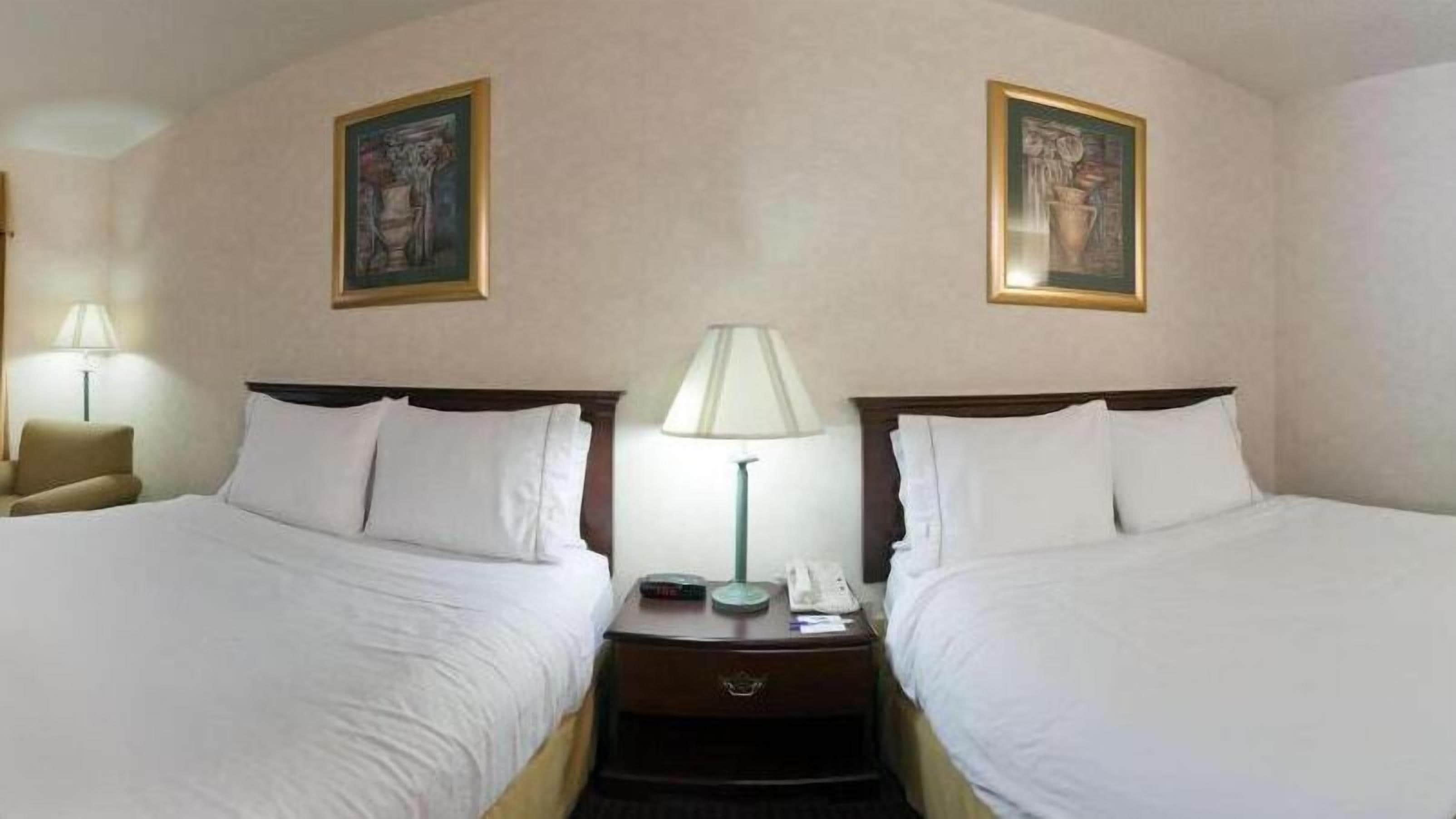 A hotel room with two beds, a nightstand with a lamp, and two framed pictures on the wall.