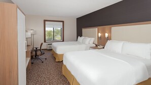 Habitación de hotel con dos camas, un escritorio con silla, una lámpara y una ventana con vistas.
