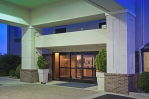 Een hotelentree met een dubbele deur, een overdekte doorgang en een gevel van baksteen.