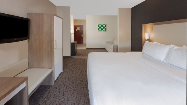 Habitación de hotel con una cama grande, televisión montada en la pared, escritorio y zona de estar.
