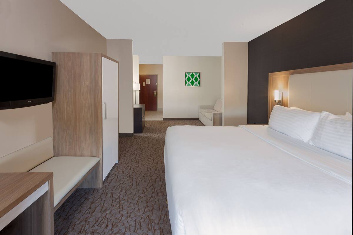 A hotel room with a large bed, a TV mounted on the wall, a desk, and a seating area.