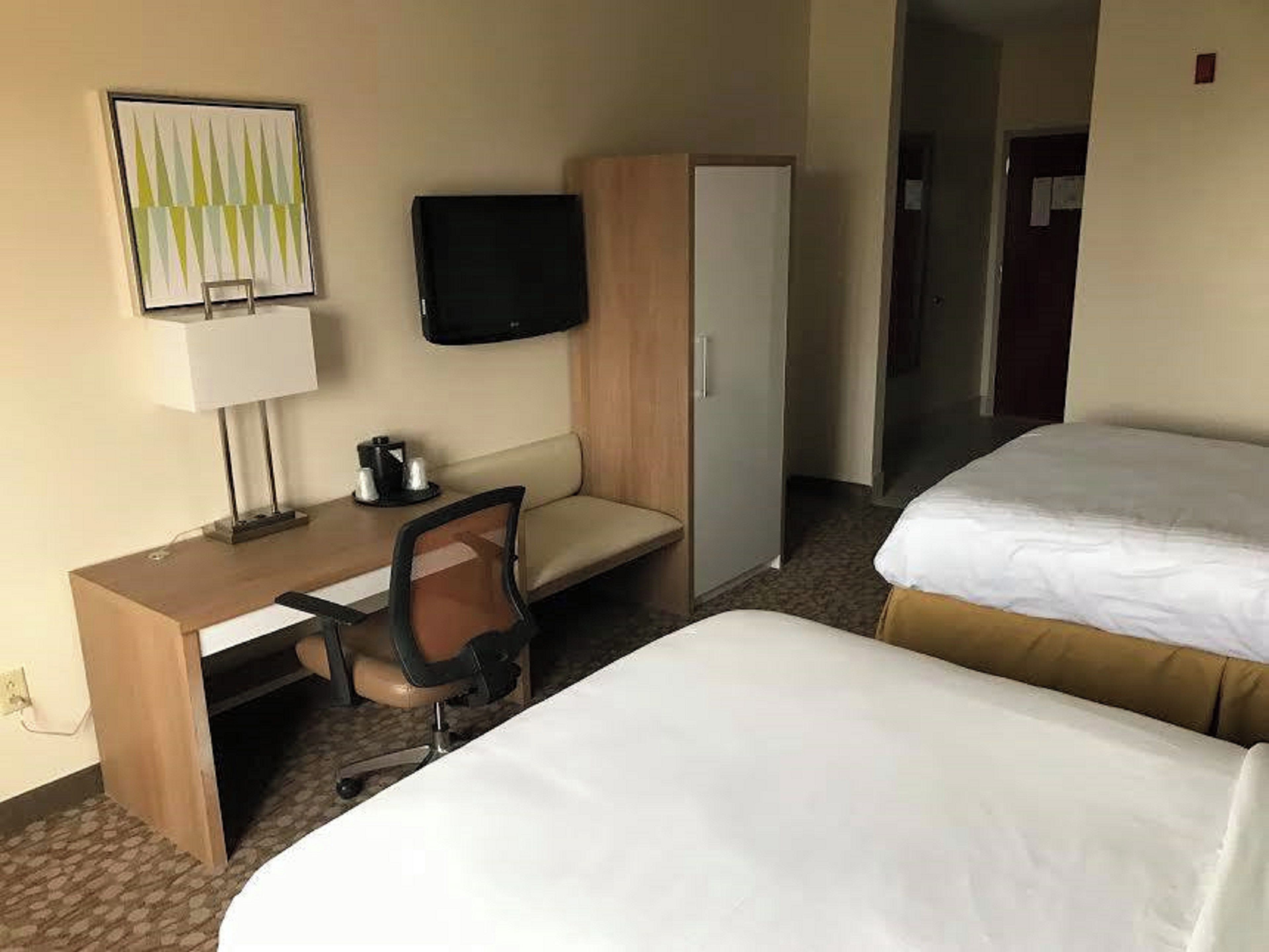 A hotel room with a desk, chair, television, wardrobe, and two beds.
