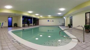 Una piscina interior con suelo de baldosas, una escalera de piscina y un cartel de prohibición de saltos.