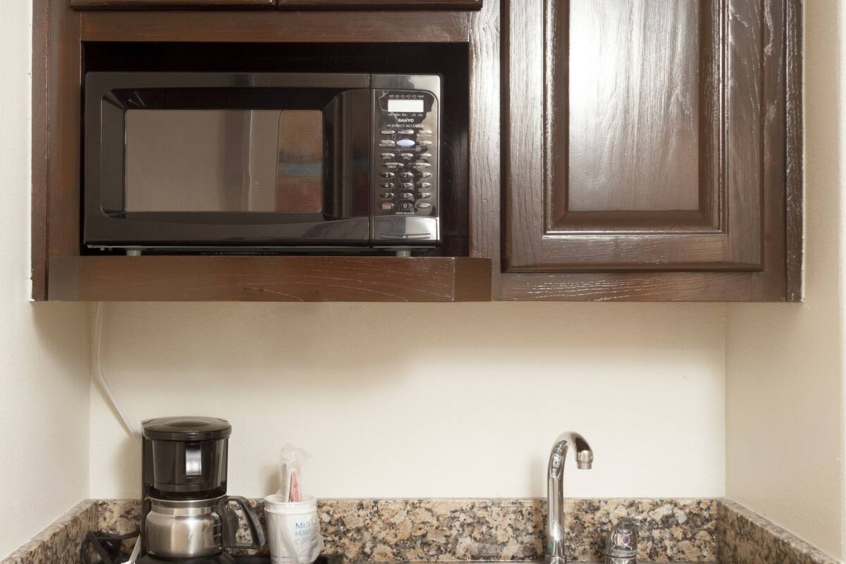 A kitchen with dark wooden cabinets, a built-in microwave, a coffee maker, and a stainless steel sink.