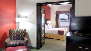 Une chambre d’hôtel avec un lit, une télévision, une chaise et une porte donnant sur une autre pièce.
