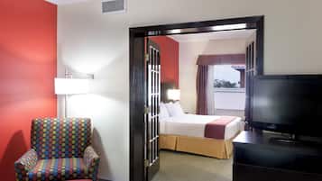 Habitación de hotel con cama, televisión, sillón y puerta que da a otra habitación.