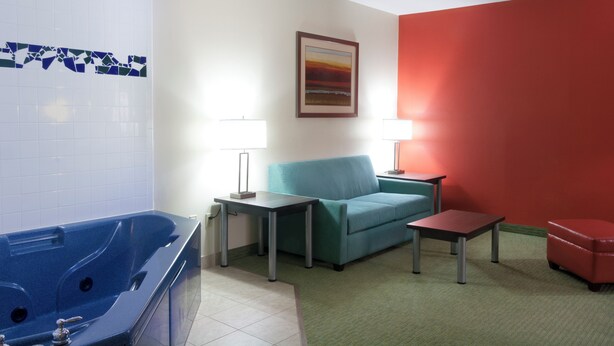 Une pièce avec une baignoire, un canapé bleu, deux petites tables et un mur rouge.