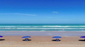Une plage avec trois parasols bleus et des chaises de plage.