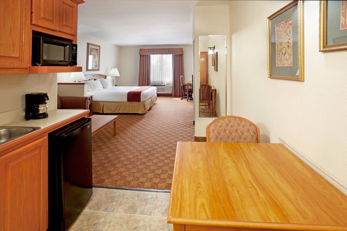Habitación de hotel con cama, escritorio, silla, microondas, cafetera y refrigerador.