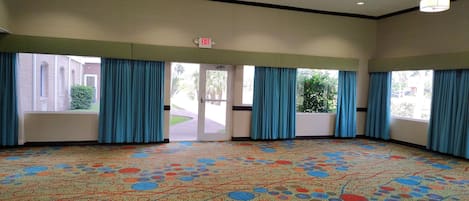 Amplia habitación con alfombra estampada, ventanas grandes con cortinas azules y múltiples luces de techo.
