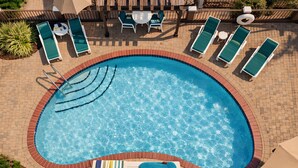 Une piscine entourée d’une allée pavée en briques, avec des chaises longues et une table à proximité.