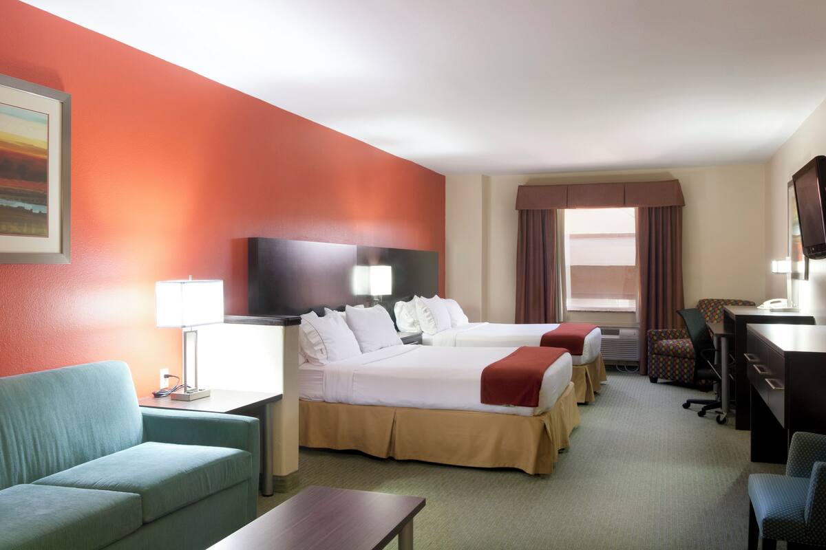 A hotel room with two beds, a desk, a chair, a TV, and a painting on the wall.