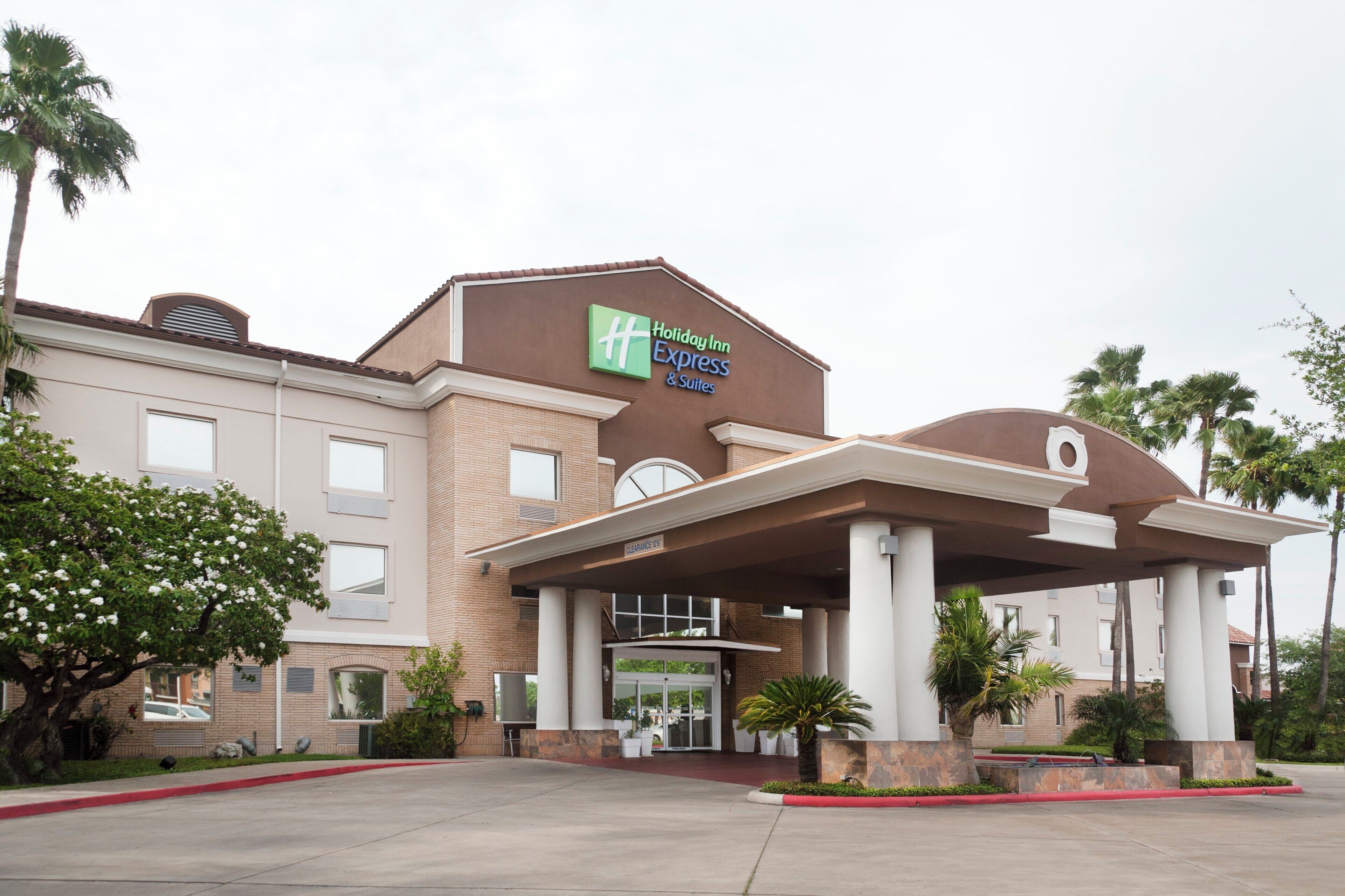 A Holiday Inn Express & Suites building with a covered entrance, brick facade, and palm trees.
